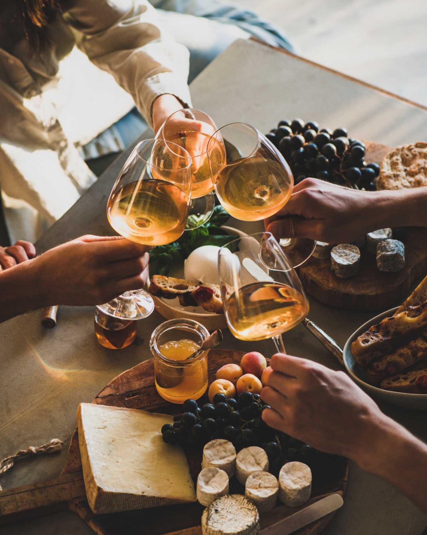 Friends gathered around a table sharing wine, cheese, and fruit